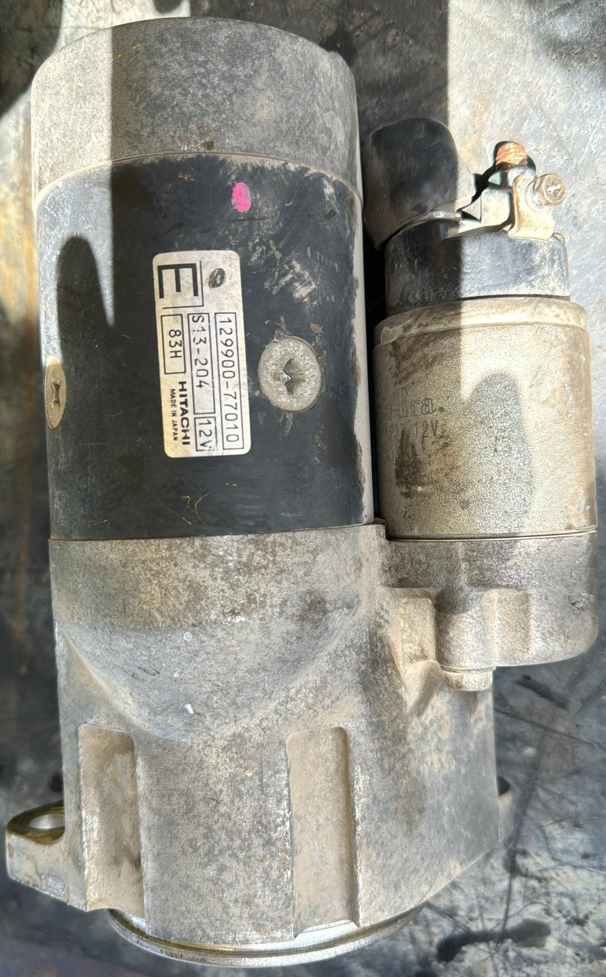 Side view of a starter body and adjacent solenoid housing, with label print 129900-77010, S13-204 and 12V visible.