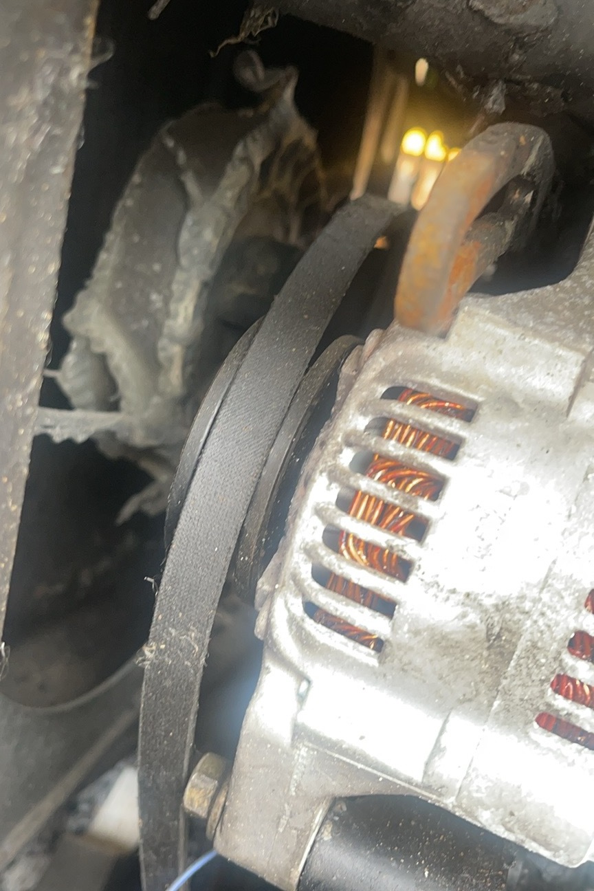 A tight installed alternator and belt view with part of the housing outside the frame.